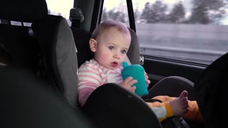 niña pequeña sentada en el asiento de bebé mientras el coche está conduciendo. bebé viajando en un asiento de coche en la parte trasera del vehículo. viaje largo en coche. niño pequeño jugando, bebiendo. turismo y viajes, concepto de viaje.
