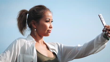 Young-woman-with-tied-back-hair-takes-selfie-outdoors-under-a-clear-blue-sky