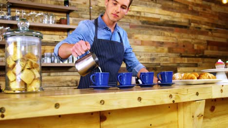 waiter pouring milk in coffee at counter