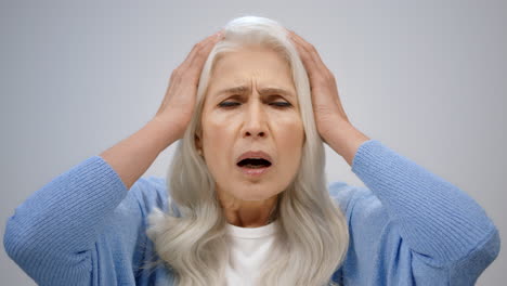 shocked senior woman crying in studio. stressed old lady grabbing head indoors.