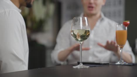 close up shot of glass of wine on table as men talk in background