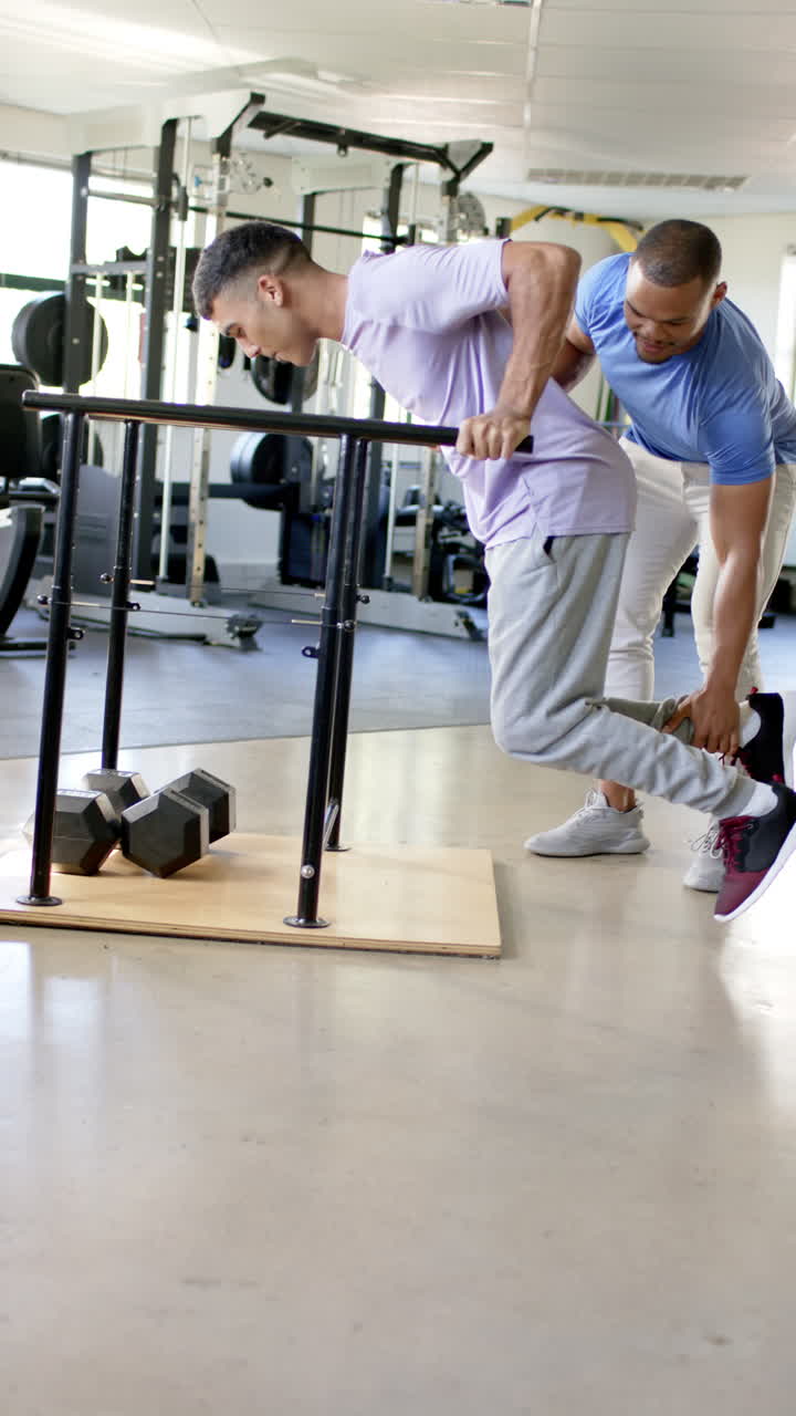Vertical video: Man in rehabilitation using parallel bars with therapist assisting in gym