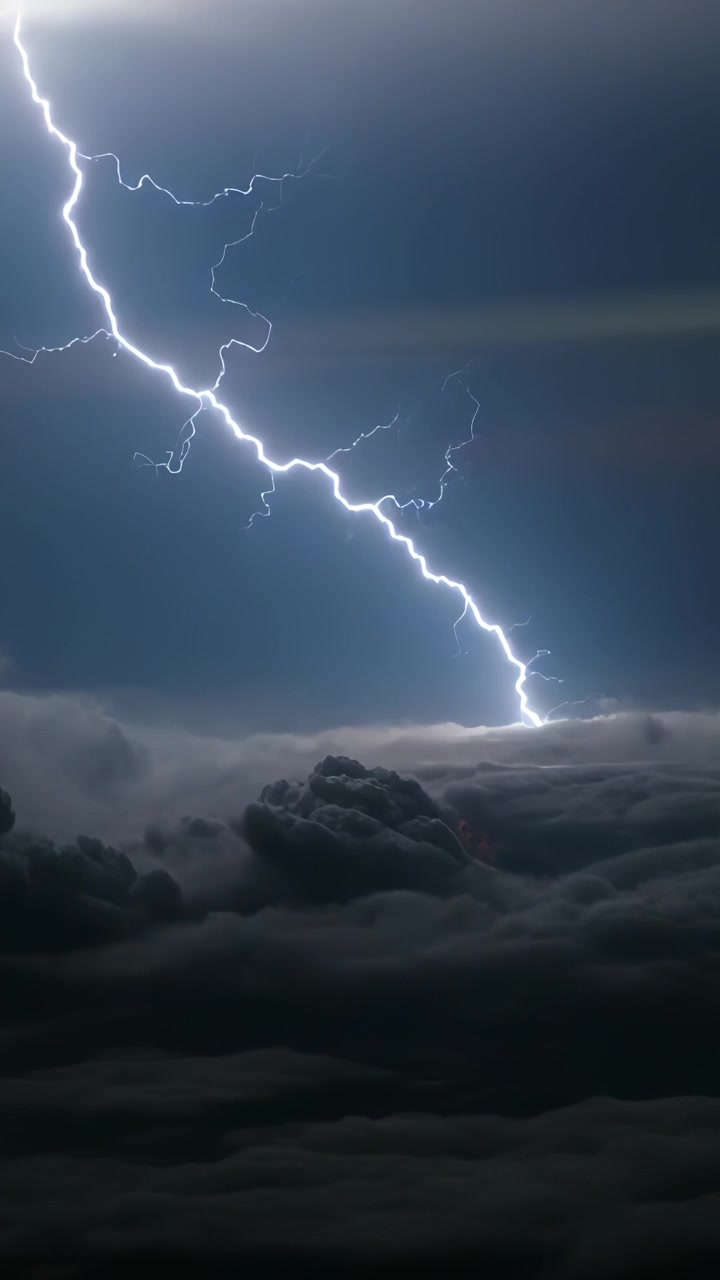 Video verticale: Fulmine lampeggiante che parte dall'alto a sinistra e colpisce le cime delle nuvole di notte, con impatto luminoso.