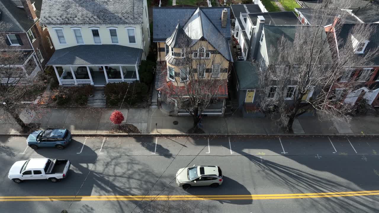 Luftfoto ovenfra av en gående fotgjenger på fortauet langs et viktoriansk hus om høsten. Solfylt dag med fargede trær og løv. Trafikk på veien i en amerikansk by.