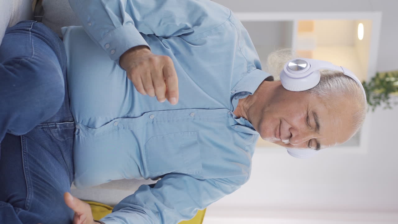 Vertikal video av glad gammel mann som lytter til musikk med hodetelefoner
