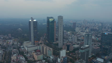 Ascending-aerial-view-of-tall-glass-skyscrapers-rising-above-modern-urban-city-center-of-Mexico-City-in-the-evening