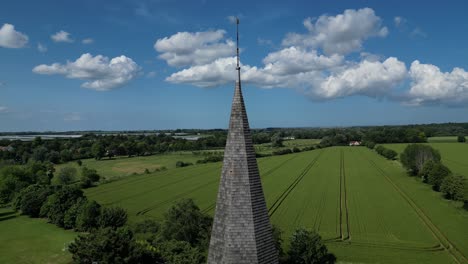 Rising-push-in-shot-of-the-spire-of-St-John-the-Evangelist-church-in-Ickham,-with-large-and-sparse-clouds-in-the-blue-sky