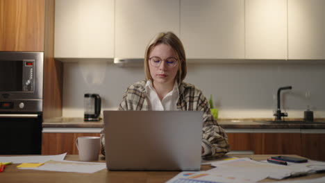 Zoomkamera:-Eine-Frau-Mit-Brille-Arbeitet-Von-Zu-Hause-Aus,-Sitzt-An-Einem-Tisch-Mit-Einem-Laptop-Und-Markiert-Mit-Einem-Filzstift-Die-Daten-In-Der-Grafik.-Fernstudent-Zu-Hause,-Um-Eine-Aufgabe-Auszuführen