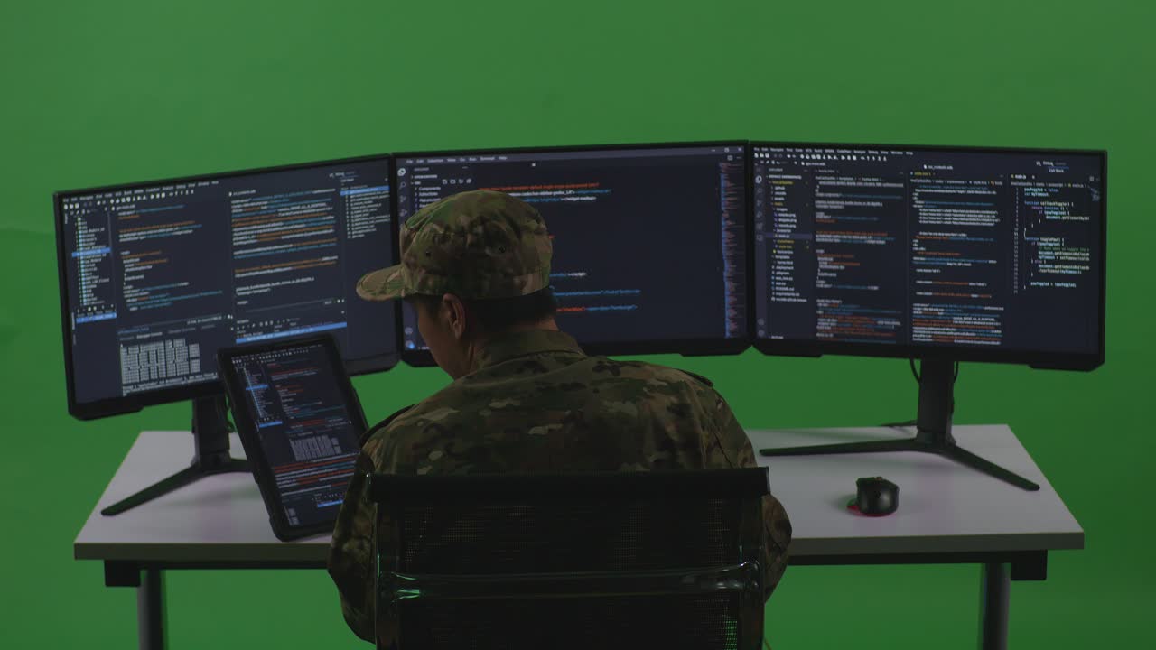Back View Of Asian Man Soldier Developer Working With Tablet While Write Code With Multiple Computer Screens In Green Screen Studio