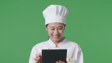 close up de la mujer asiática chef sonriendo y señalando a la tableta en su mano mientras estaba de pie en el estudio de fondo de la pantalla verde