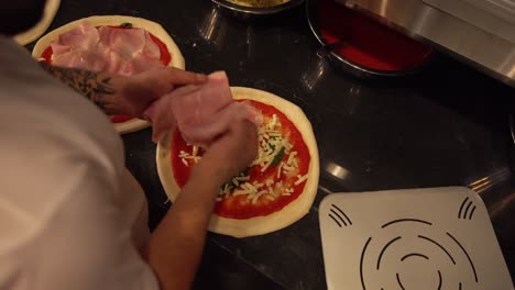 chef adding sliced ham pieces on pizzas in restaurant kitchen. overhead view of fresh pizza preparation in restaurant