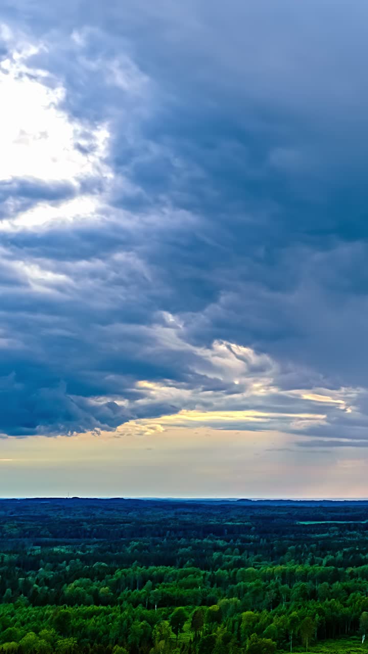 Dark rain clouds slowly cover a wooded area in an aerial time lapse shot