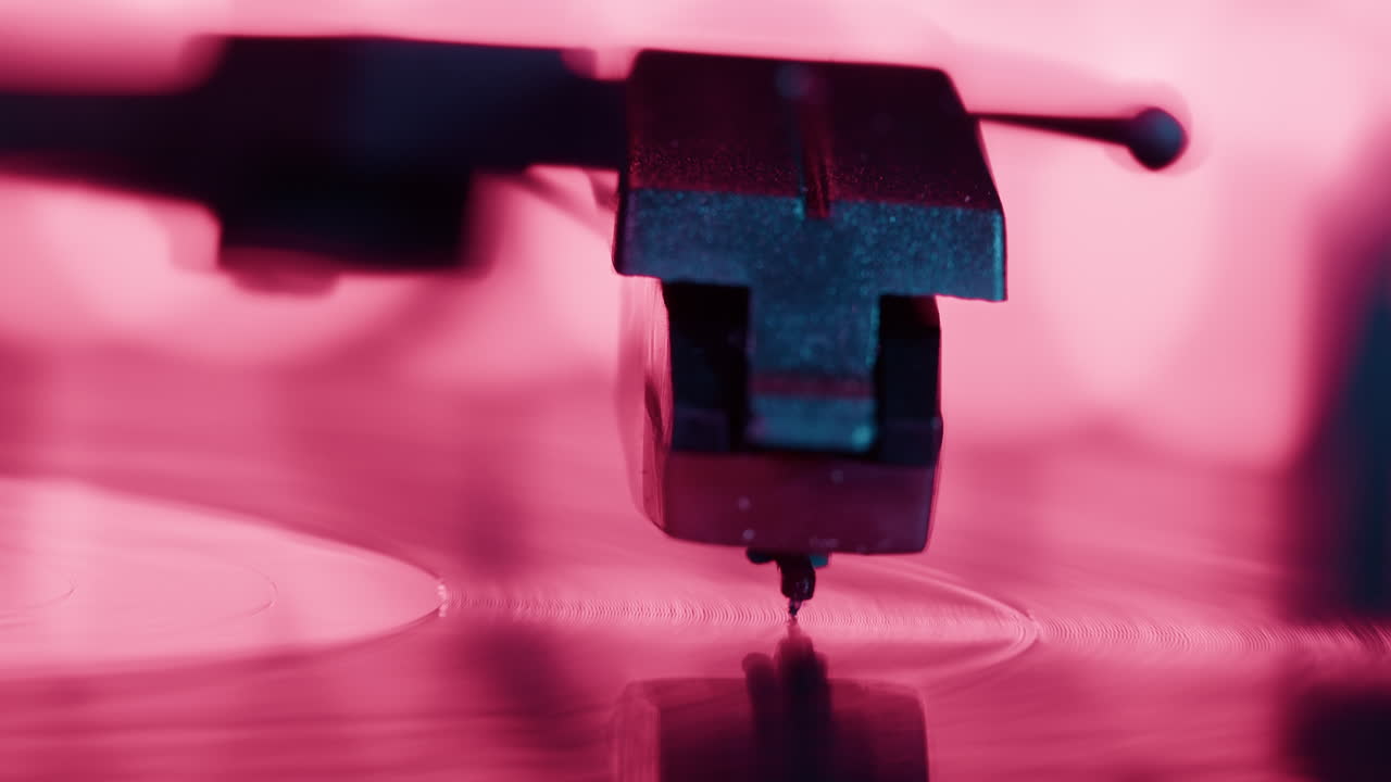 Primo piano della puntina di un giradischi che riproduce un disco in vinile con luce rosa