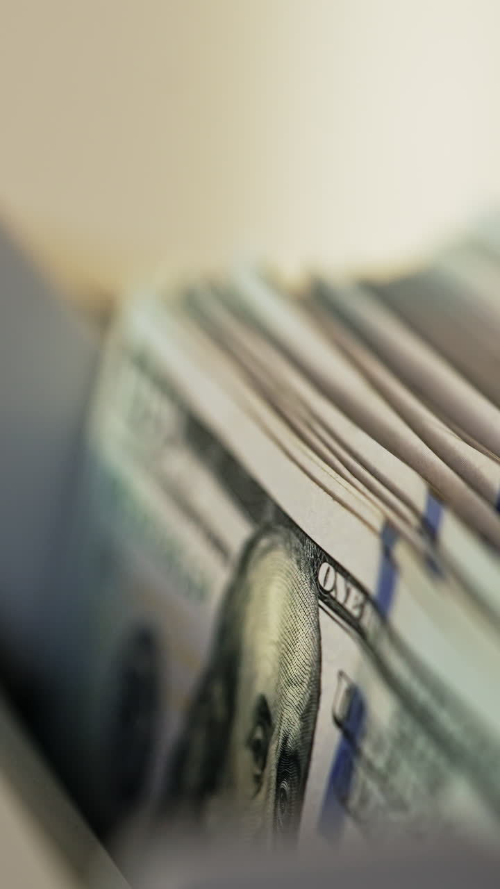 Male hand placing money into counting slot of cash machine. One hundred dollar bills quickly disappearing in the apparatus. Close up. Vertical video