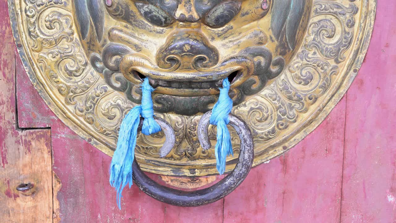 Close-up of a brass door knocker at Erdene Zuu Monastery, Mongolia. The ornate lion head with blue ceremonial scarves highlights the intricate detail of the ancient temple