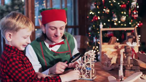 santa claus elf is playing with a boy with a new year's wooden toy near a christmas tree