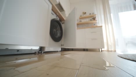 water leaking from a washing machine in a contemporary kitchen setting, showing a puddle on wooden flooring