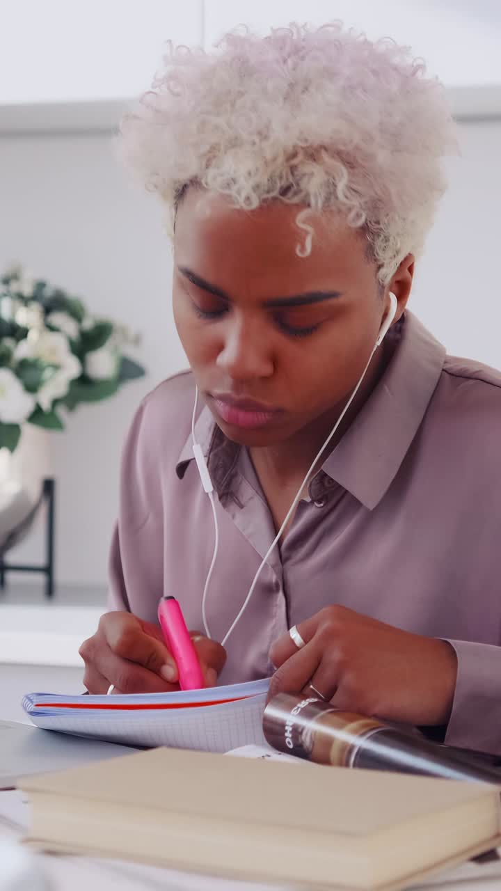 Giovane donna concentrata con gli auricolari che scrive appunti su un quaderno con un laptop