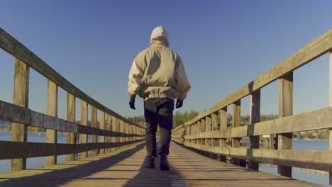 Person,-Die-Im-Herbst-über-Einen-Holzsteg-Mit-Wasser-Im-Hintergrund-Läuft