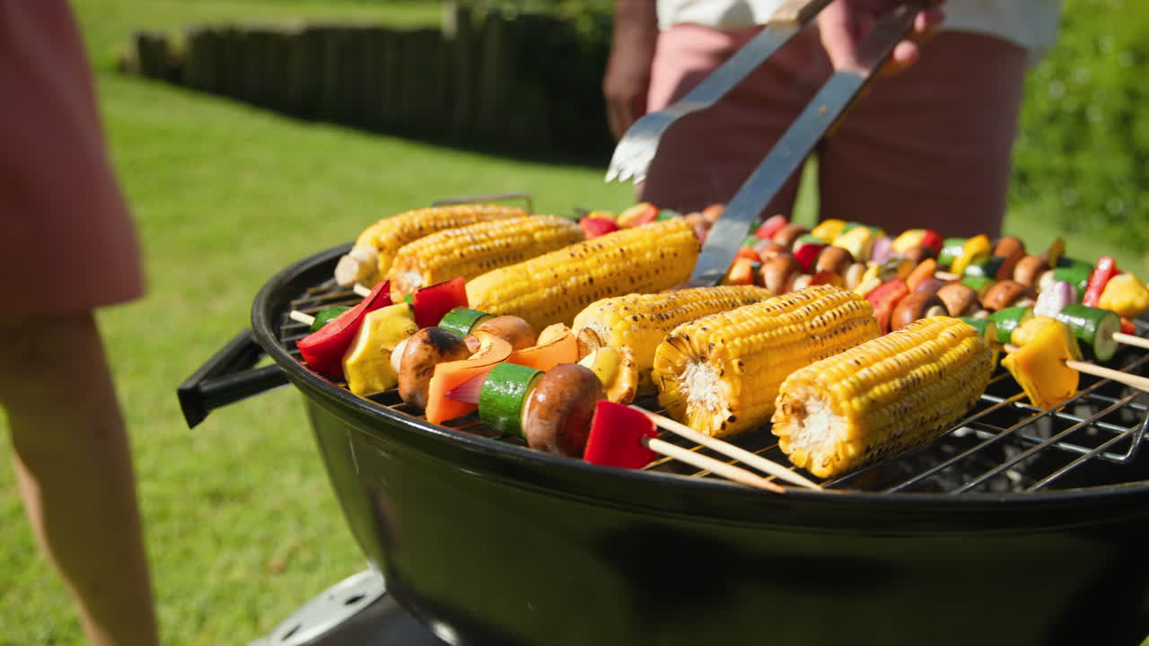 Grilling corn and vegetables on barbecue grill in sunny backyard gathering