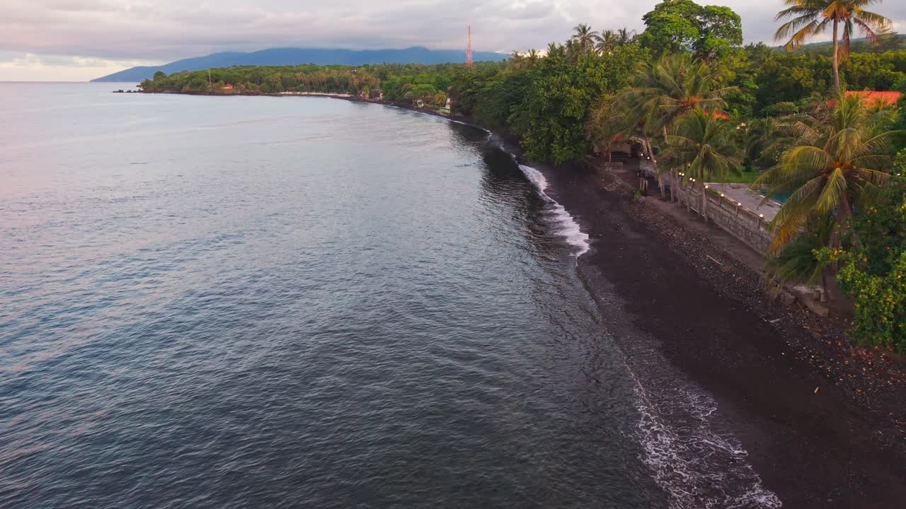 Low altitude reverse drone flight above a black volcanic pebble beach in Indonesia