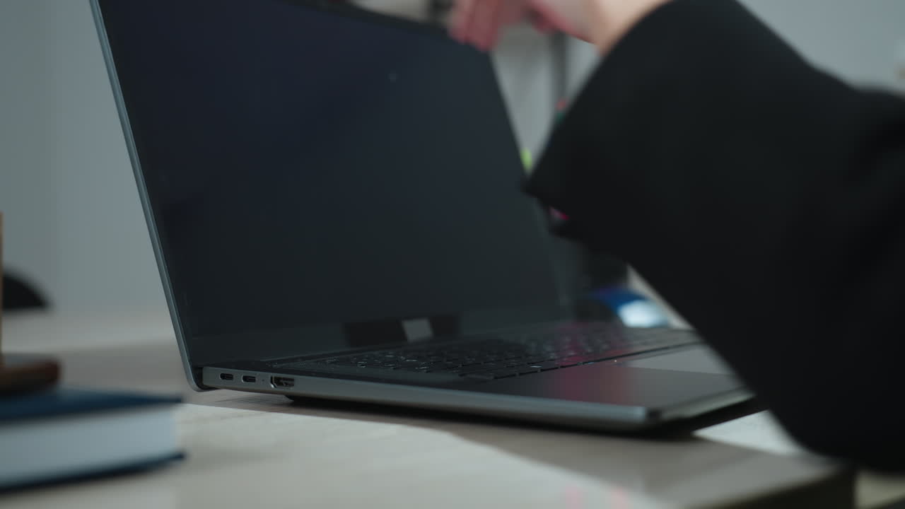 Close up of woman with glossy manicured nails gently opening laptop on office desk, with blurred view of colorful pens in container and background shelf