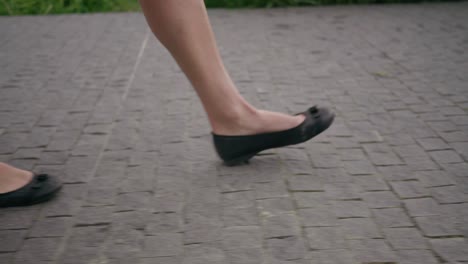 Detail-follow-shot-of-women's-legs-walking-in-ballerinas-on-the-grey-pavement-to-the-right