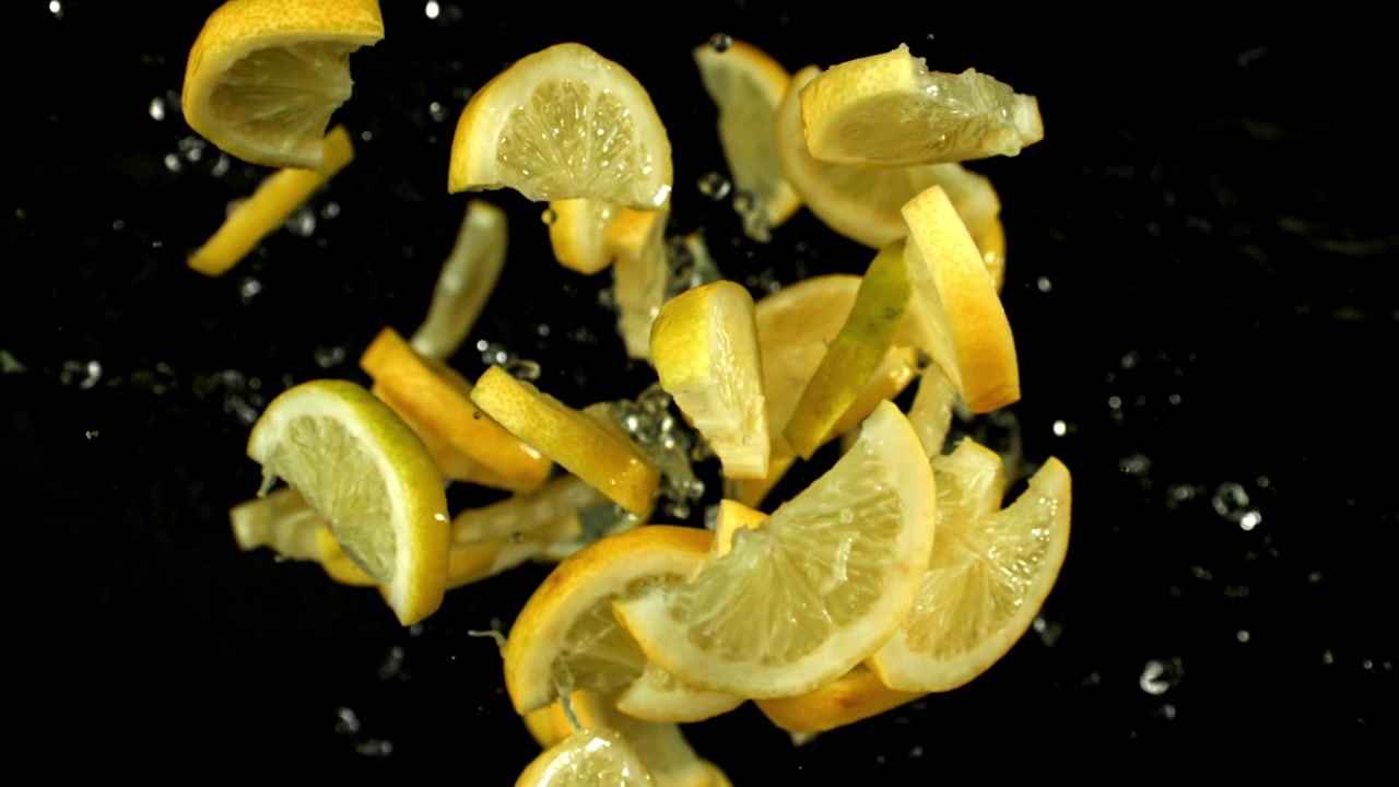 Fette di limone fresche che cadono al rallentatore con schizzi d'acqua