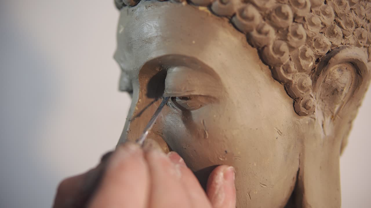 Portrait of clay Buddha's statue face, artist works with details using spatula