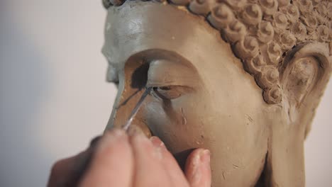 Portrait of clay Buddha&#039;s statue face, artist works with details using spatula