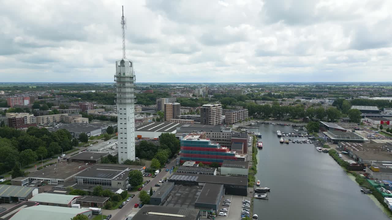 Detailed drone view circling a modern telecom tower in Alphen aan den Rijn with surrounding buildings and marina