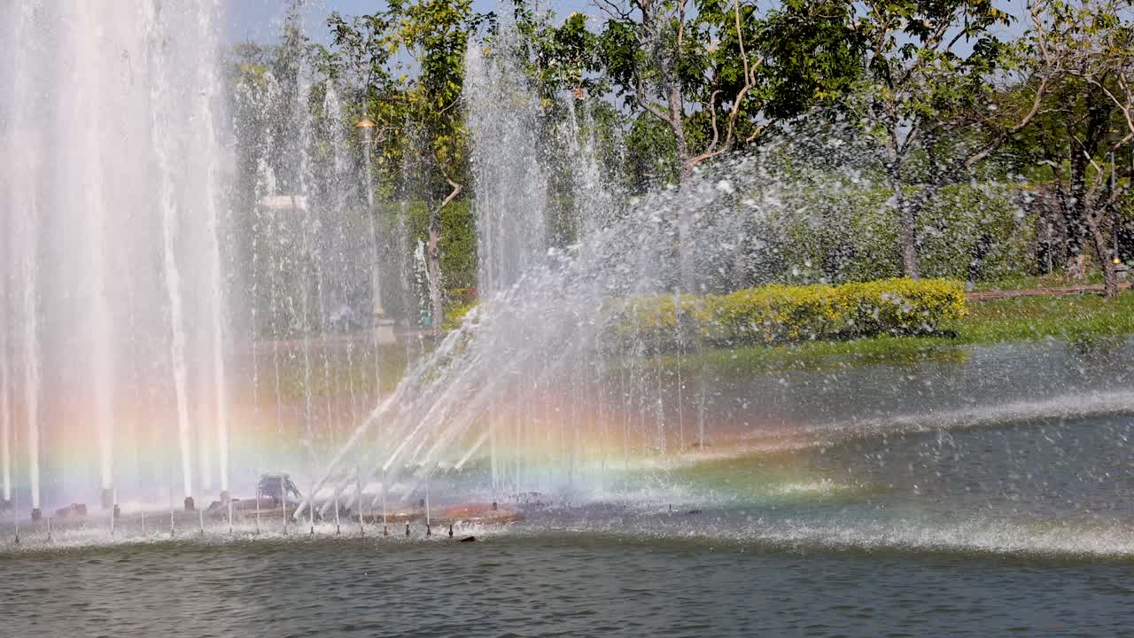 Colorful rainbow forms in fountain spray at park