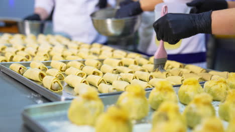unbaked croissants being prepared for baking in oven. bakers cover the pastry with liquid. close up.