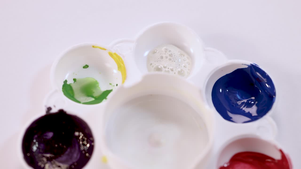 Hand squeezes paint into palette wells under bright lighting, preparing for color mixing and painting