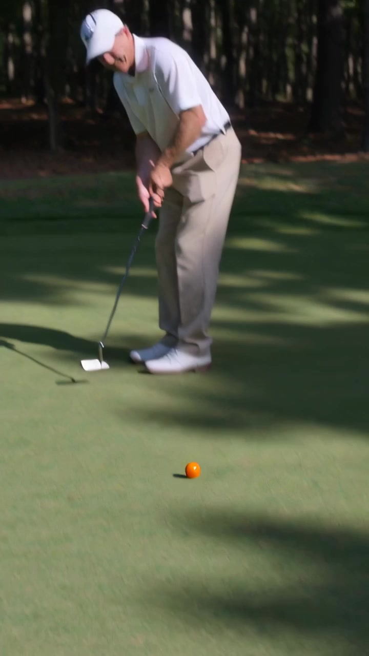 Vertical video: Golfer lining up, putting with putter on green rolling orange ball, cap, copy space