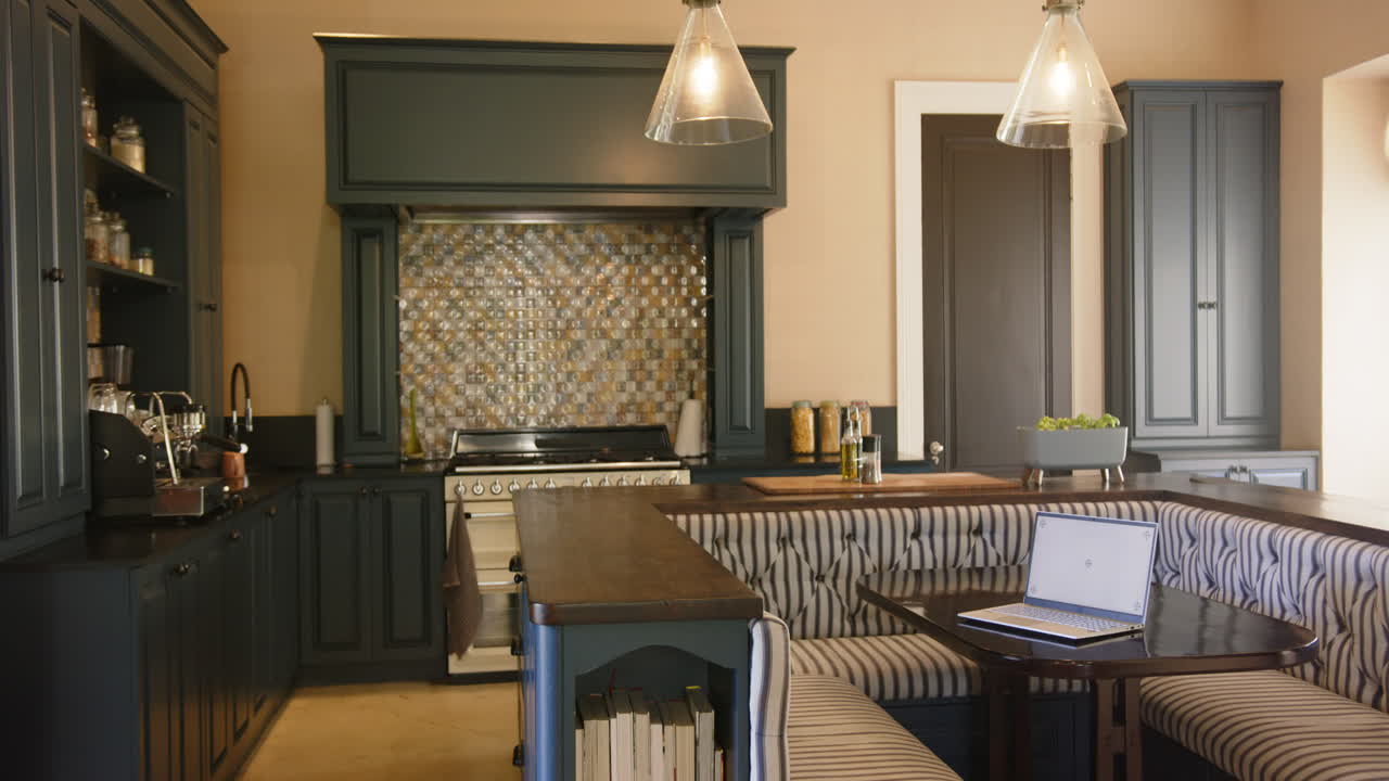 Laptop on table in modern kitchen with striped seating and built-in bookshelves, copy space