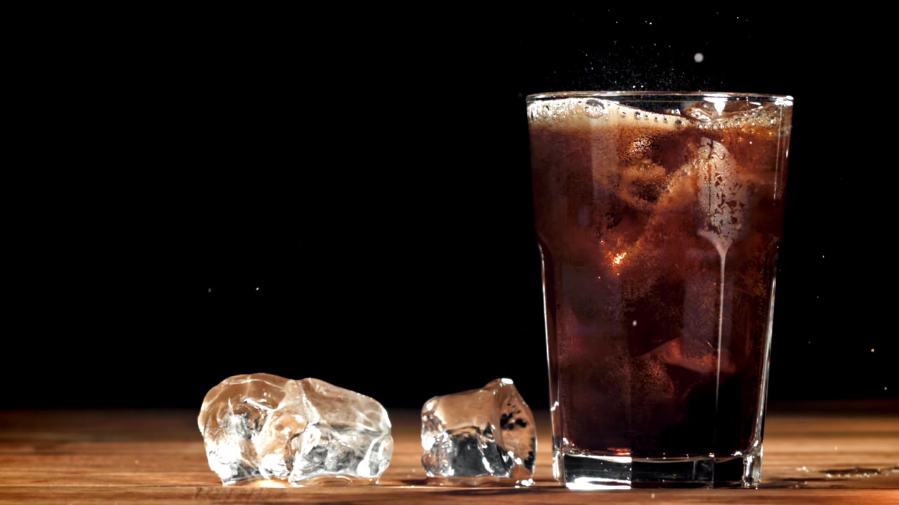 Bicchiere rinfrescante di cola con cubetti di ghiaccio su un tavolo di legno