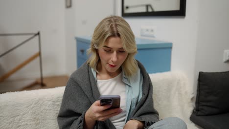 Smiling-girl-sitting-on-sofa-taking-fries-and-use-mobile,-reading-news