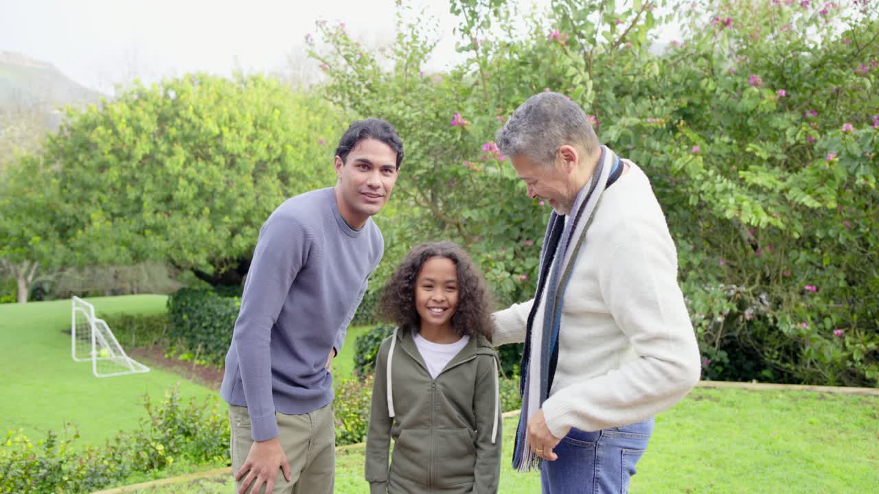 Diverse family straightening scarf before posing, pointing camera, wrapping arm around boy on lawn