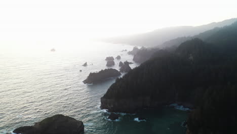 aerial view backwards over the misty coast of oregon, hazy sunrise in usa