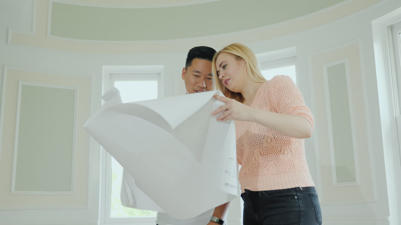 젊은 다민족 가족 부부가 수리가 가능한 실내 새 집 프로젝트를 연구하고 있습니다.