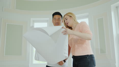 A-Young-Multi-Ethnic-Family-Couple-Is-Studying-A-Project-Of-A-New-Home-Indoors-With-Repairs