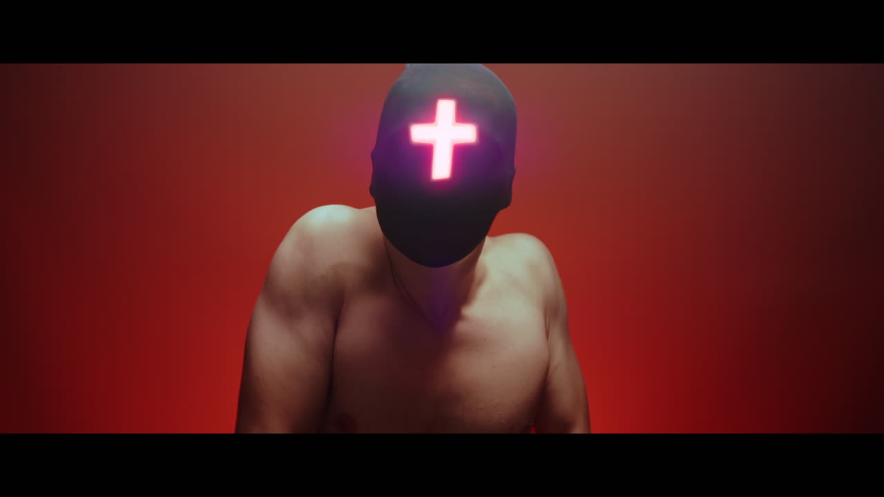 Masked man with cross of light glowing on his face moves slowly