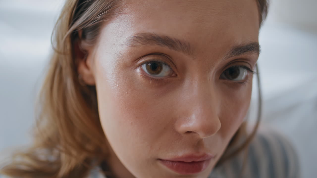 Sad woman eyes looking camera in bedroom closeup. Portrait of gentle young lady