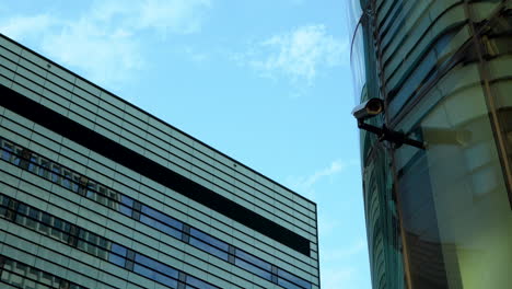 modern buildings intersecting at an angle with a security camera in the foreground against a blue sky
