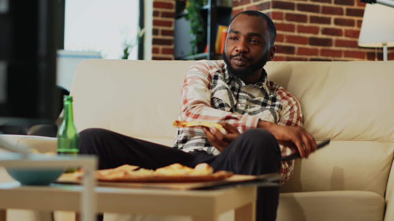 African american guy eating pizza at television