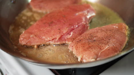 boneless, skinless chicken breasts seasoned and sizzling in oil in a skillet on the stove - slow motion