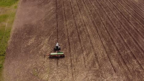 aerial birds eye shot of industrial tractor plowing agricultural farm field during sunny day in argentina