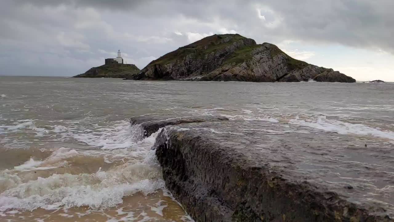 olas en cámara lenta rodando con el fondo del faro de la isla en un día ventoso