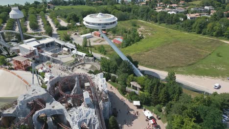 Roller-coaster-swoops-down-track-as-visitors-walk-pathway-at-midday-below-in-gardaland-Italy-park